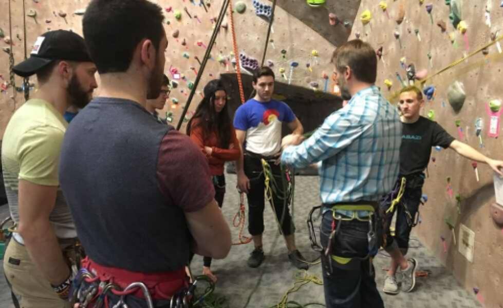 a group of climbers gathered around an instructor, watching intently as a new skill is demonstrated.